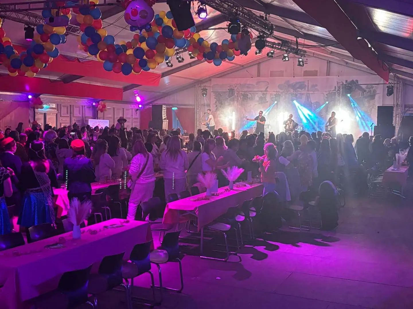 Abendveranstaltung im Festzelt Brand: Band auf der Bühne, volle Tischreihen, Ballongirlanden unter dem Zeltdach